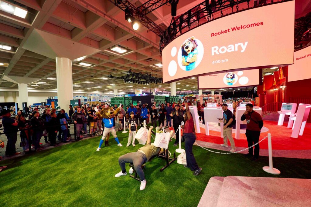 celebrity bench pressing with crowd behind him at Rocket Mortgage booth from Super Bowl Fan Experience