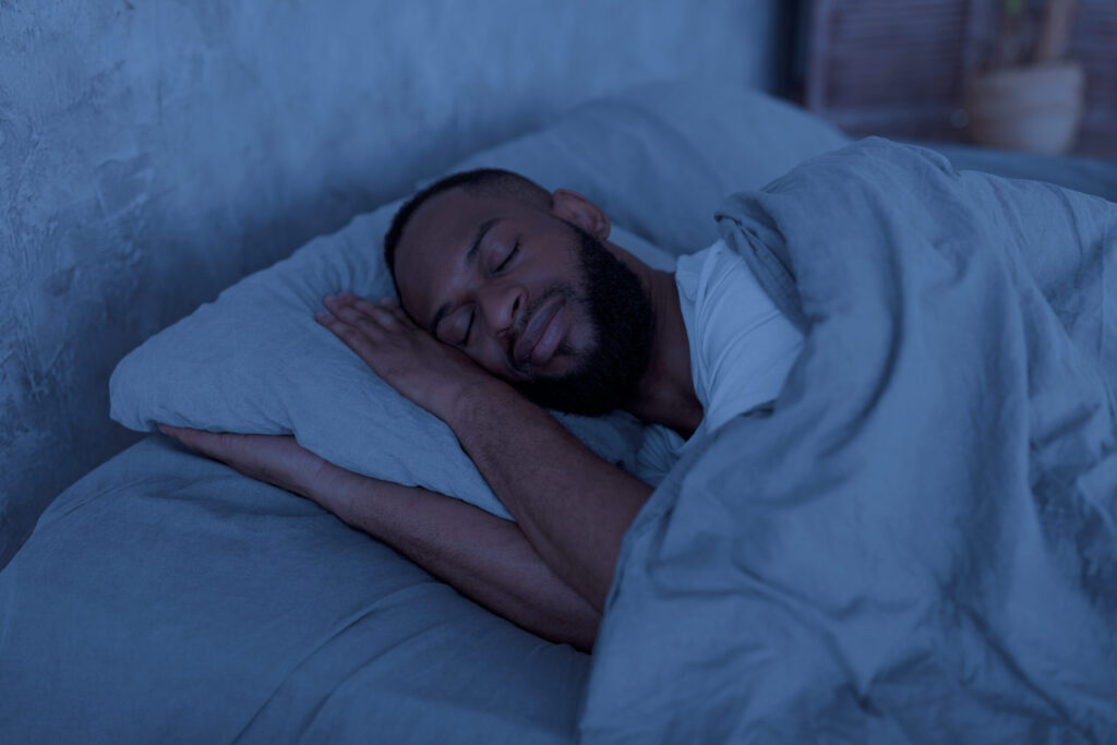 happy young well-slept African American man lying in bed with closed eyes