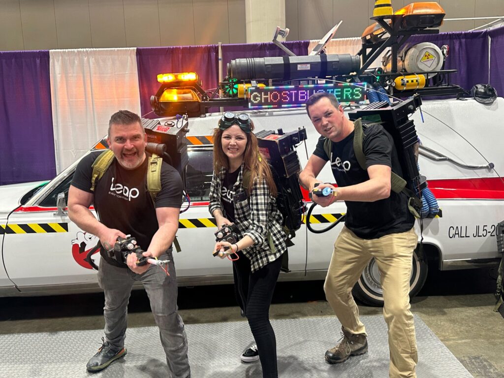 three team members in front of ghostbusters car