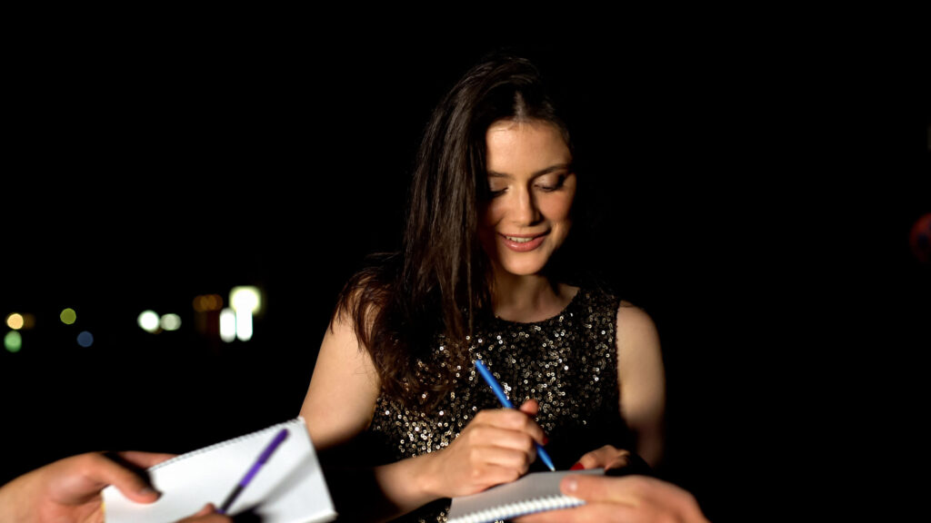 Famous woman signing autographs in fans notebooks at evening party