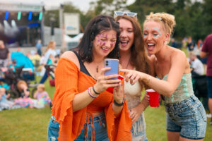 girls at a music festival laughing while looking at a phone