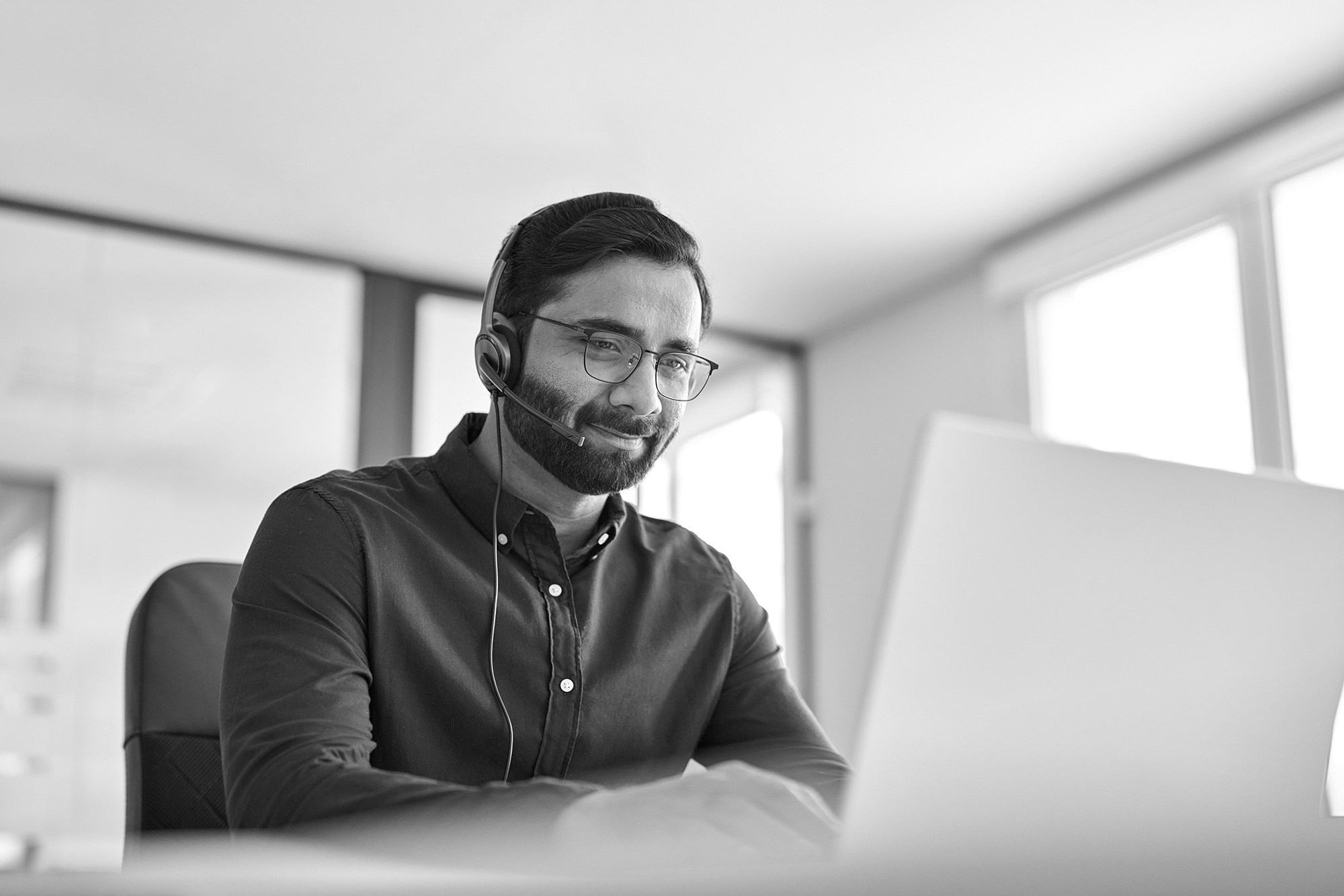 Professional Indian representative wearing headset working on customer support service, having conversation with client using a laptop computer  and working in an office.
