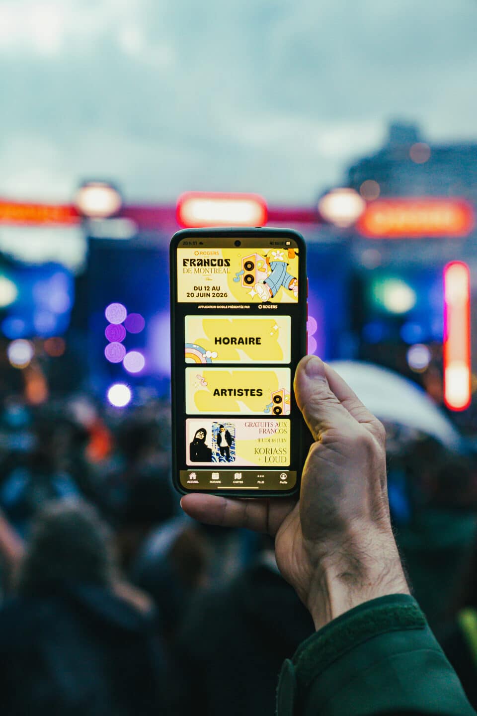 person holding up festival event mobile app in front of music stage