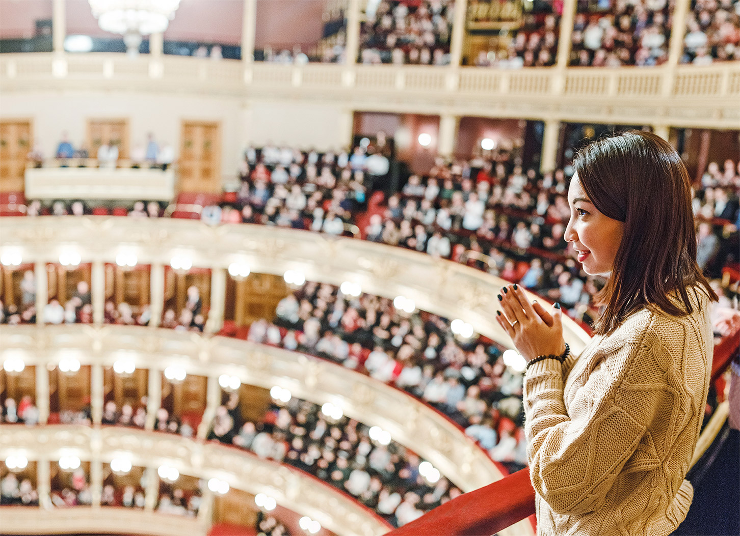 A woman applauding while standing over a performance theatre balcony