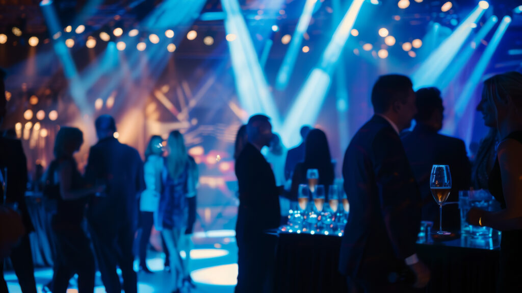 A lively party scene with blue lighting, where people are socializing, and glasses of wine are prominently displayed.