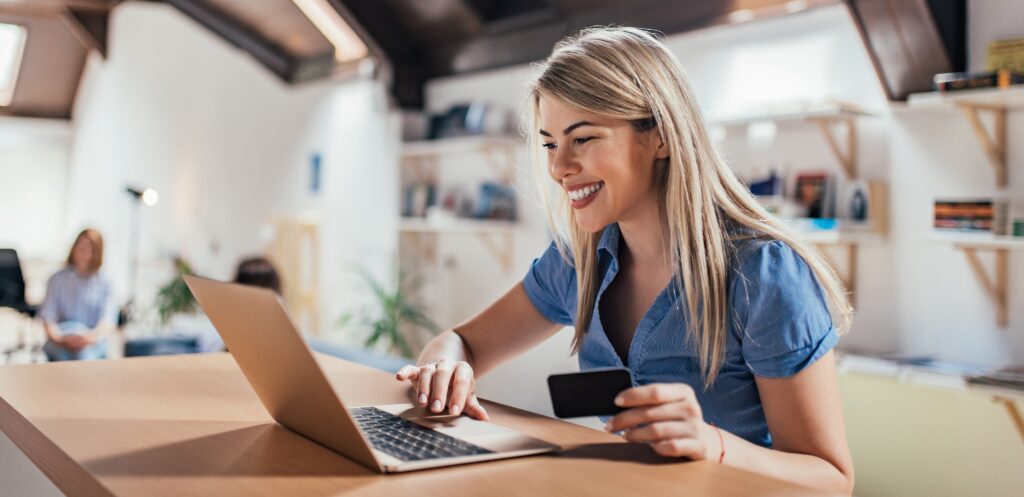 girl smiling at her laptop as she holds her credit card to make an online donation