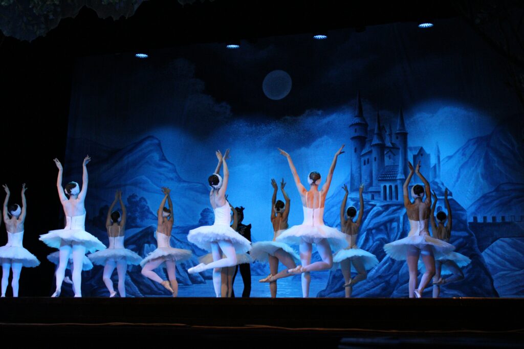 line of ballerinas in white dresses dancing in a dimly lit blue background