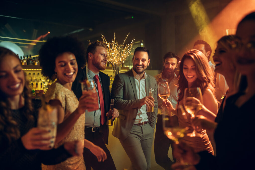 group of young people partying and holding drinks at an after party from a show in a dimly lit venue